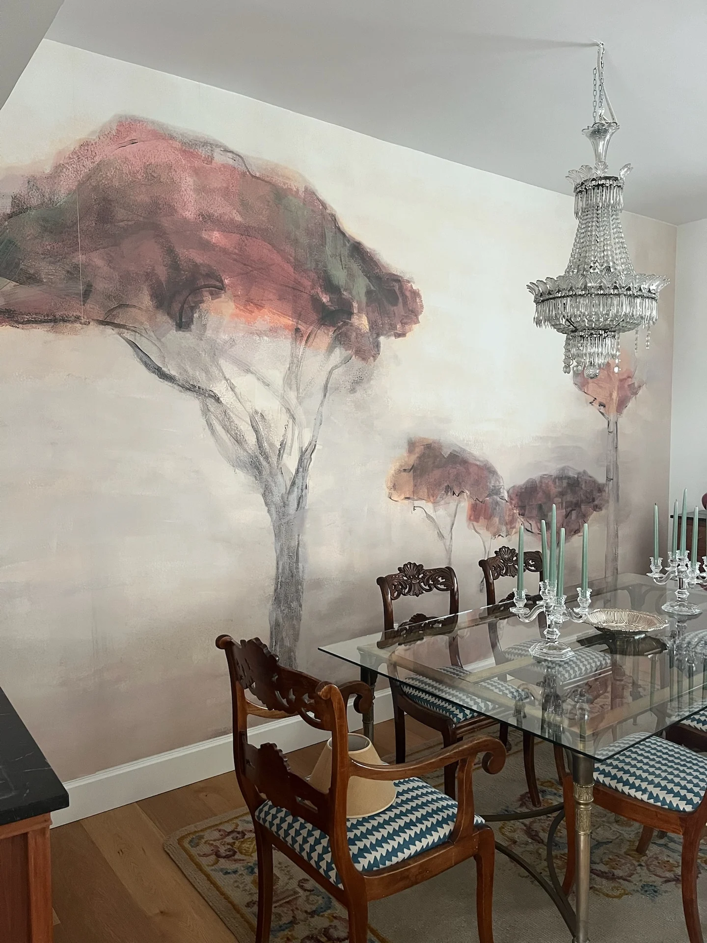 Comedor con mural, lámpara de cristal y sillas clásicas retapizadas.
